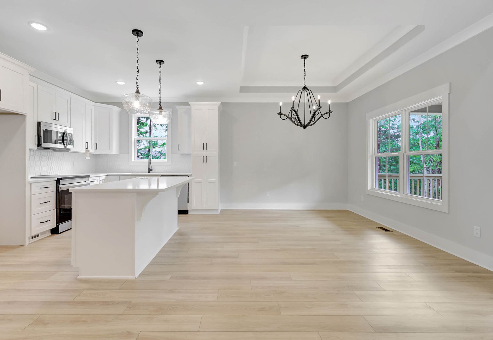 An empty kitchen with white cabinets and hardwood floors in a new home.