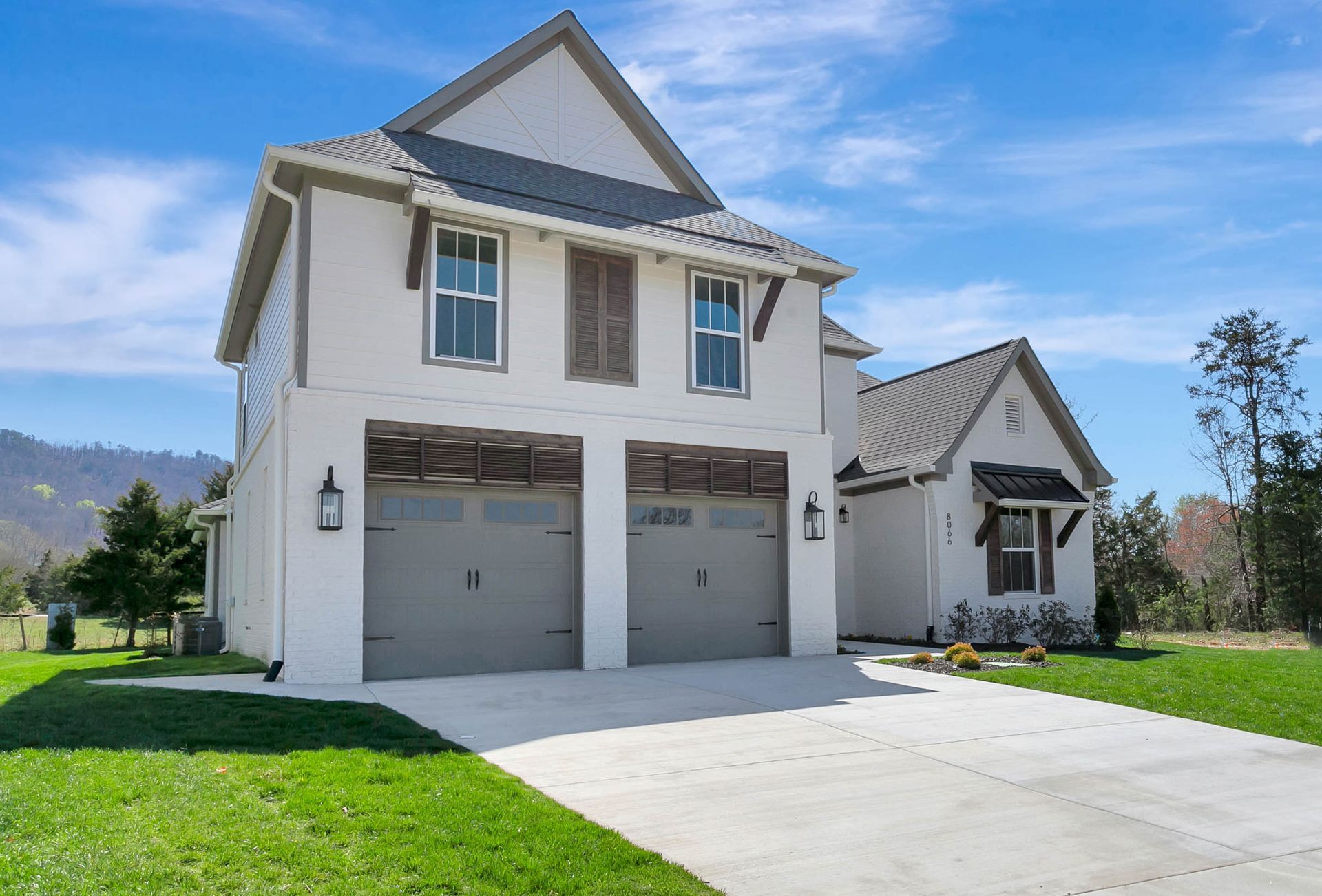 A white house with two garage doors is sitting on top of a lush green field.