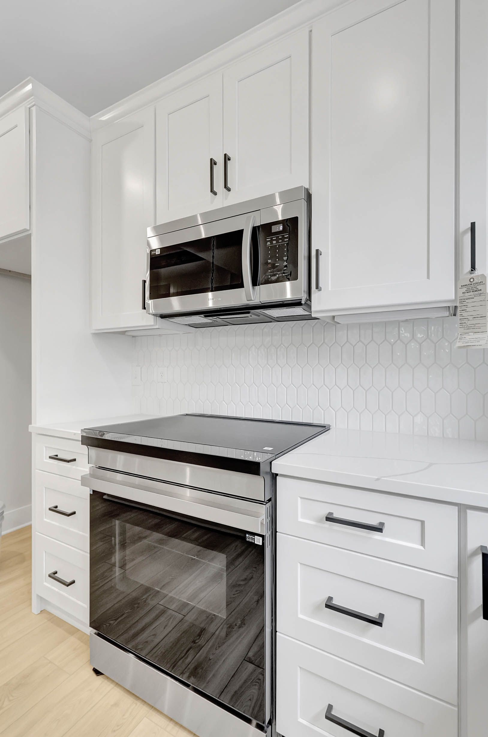 A kitchen with white cabinets , stainless steel appliances , a stove and a microwave.