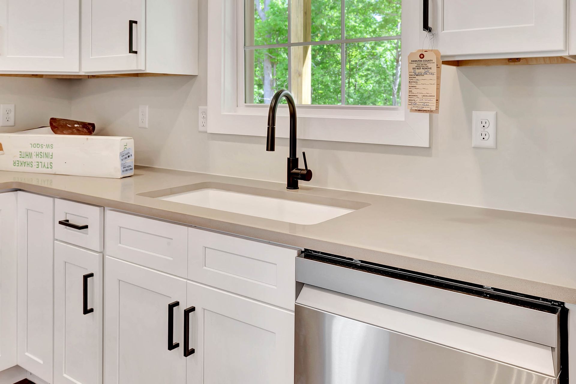 A kitchen with white cabinets , a sink , a dishwasher , and a window.