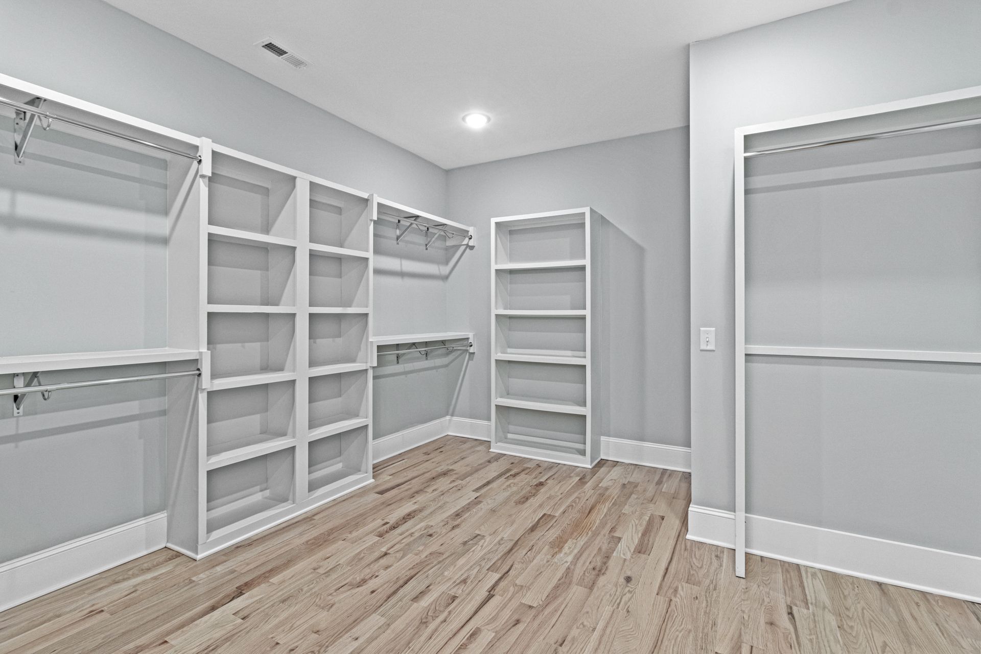 an empty walk in closet with hardwood floors and white shelves .