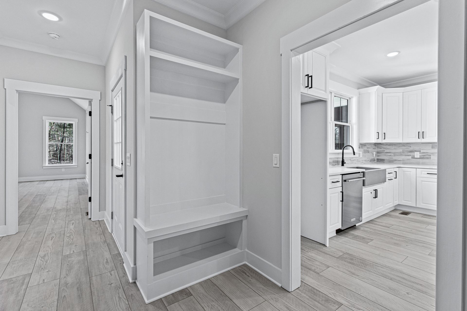 a hallway in a house with white cabinets and hardwood floors leading to a kitchen .