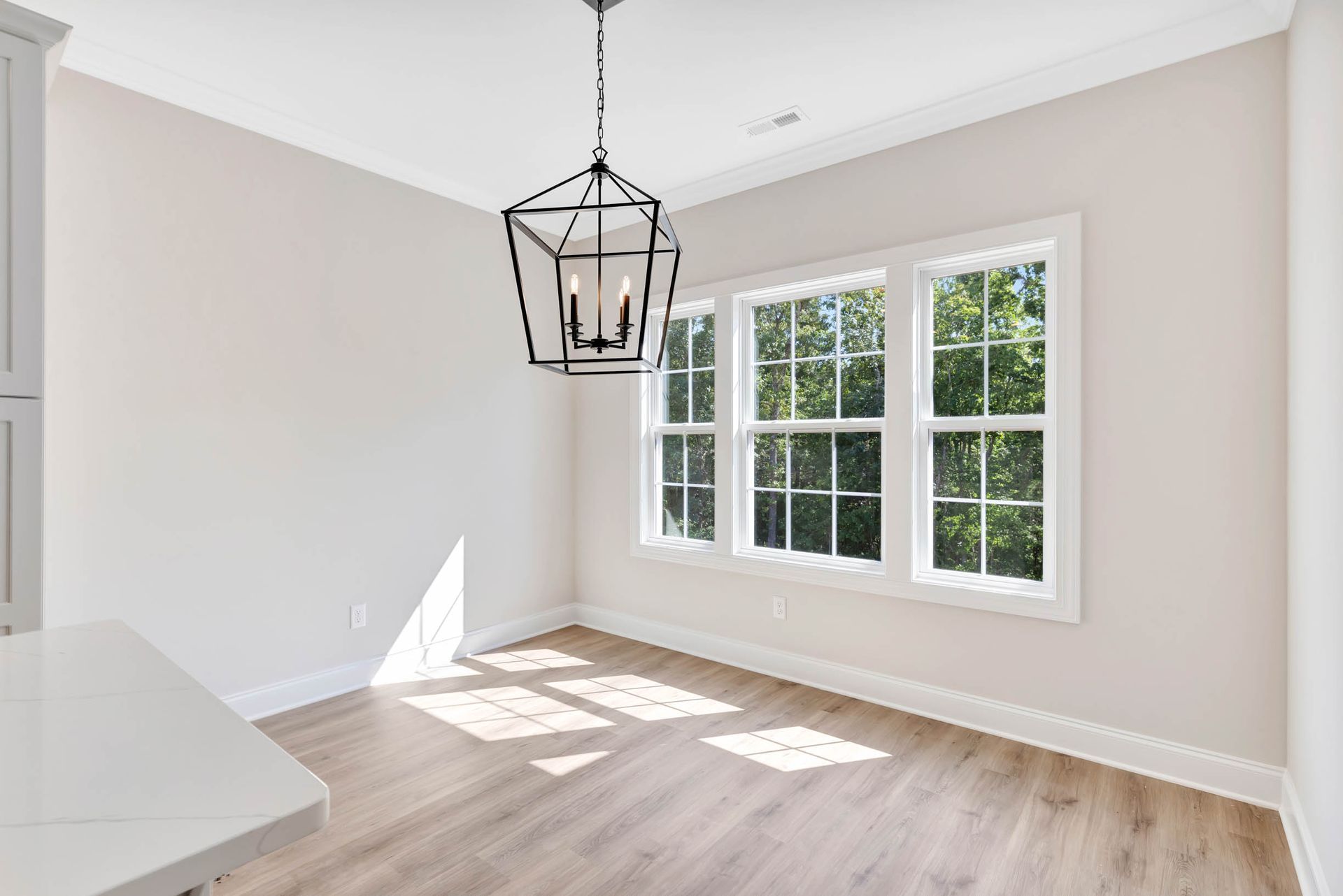 An empty dining room with hardwood floors and a chandelier hanging from the ceiling.