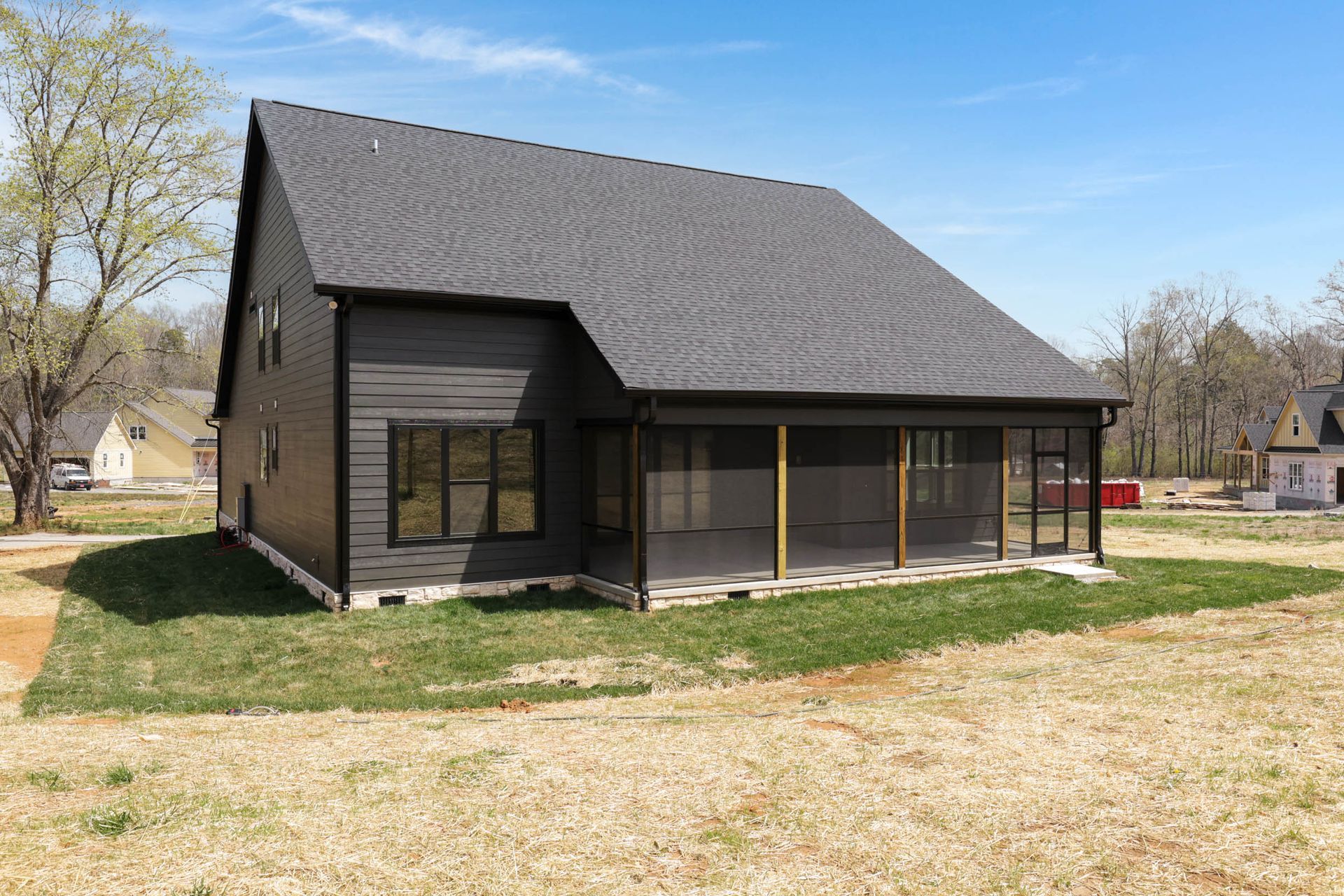 A black house with a screened in porch is sitting in the middle of a grassy field.