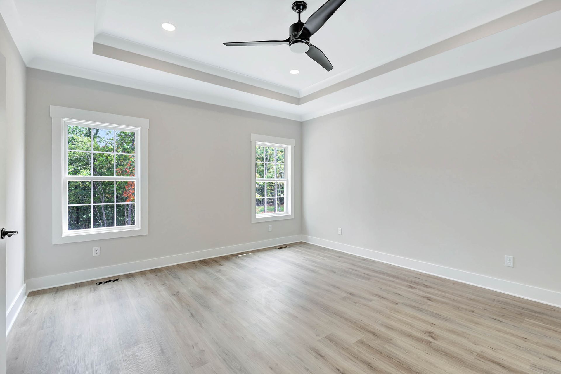 An empty room with a ceiling fan and two windows.
