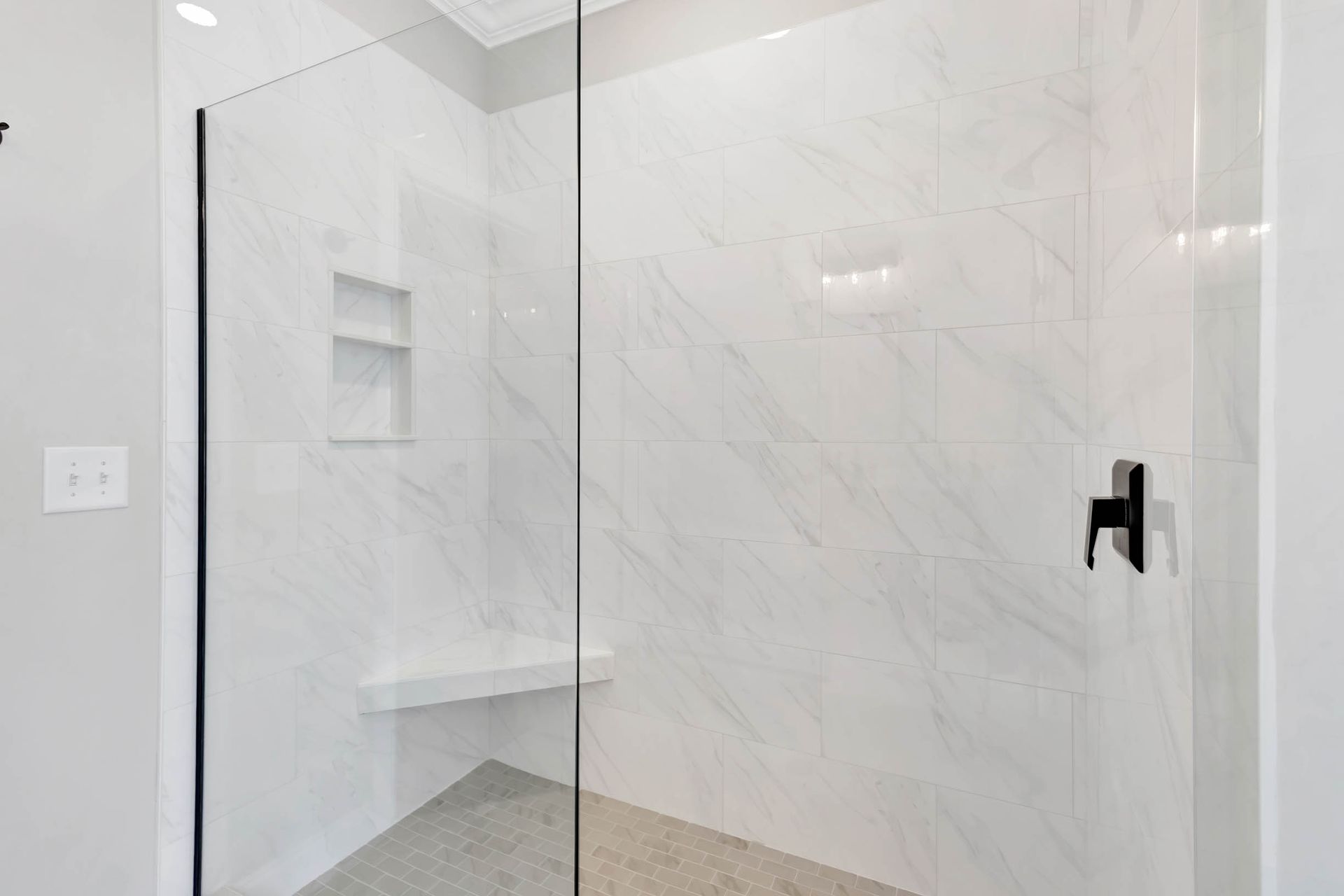 A walk in shower with a glass door and a bench.