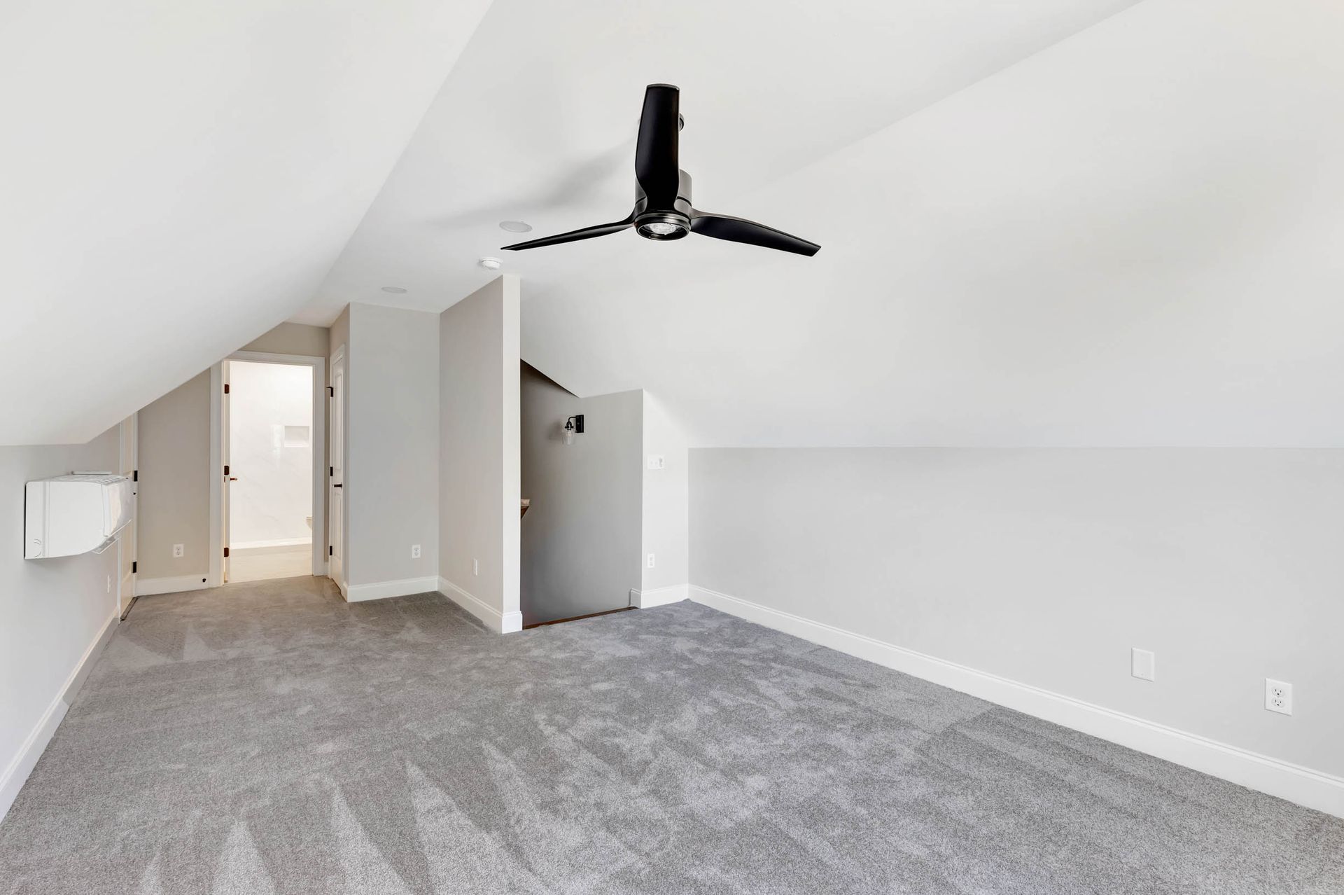 An empty room with a ceiling fan and a gray carpet.