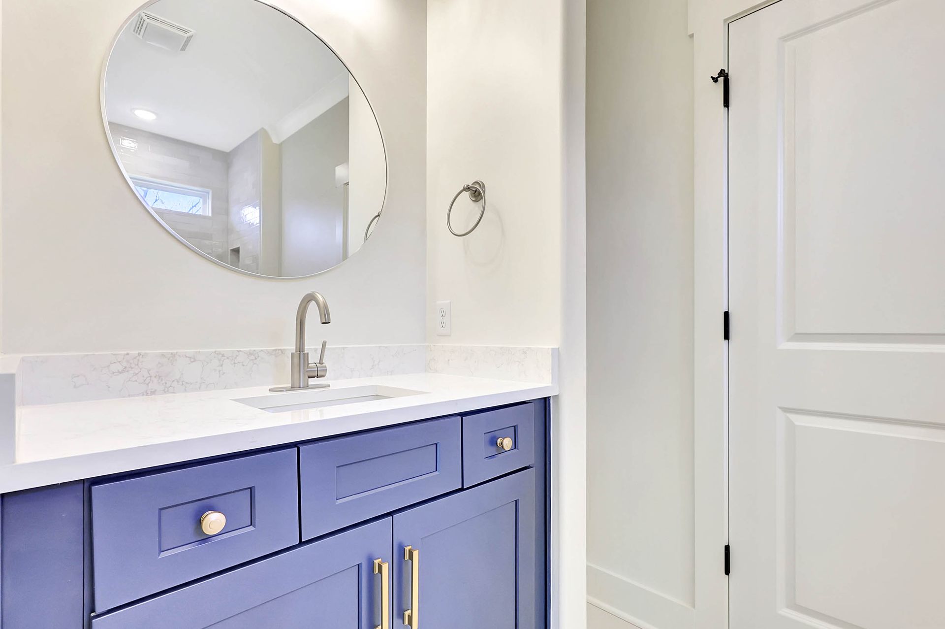 A bathroom with blue cabinets , a sink and a mirror.