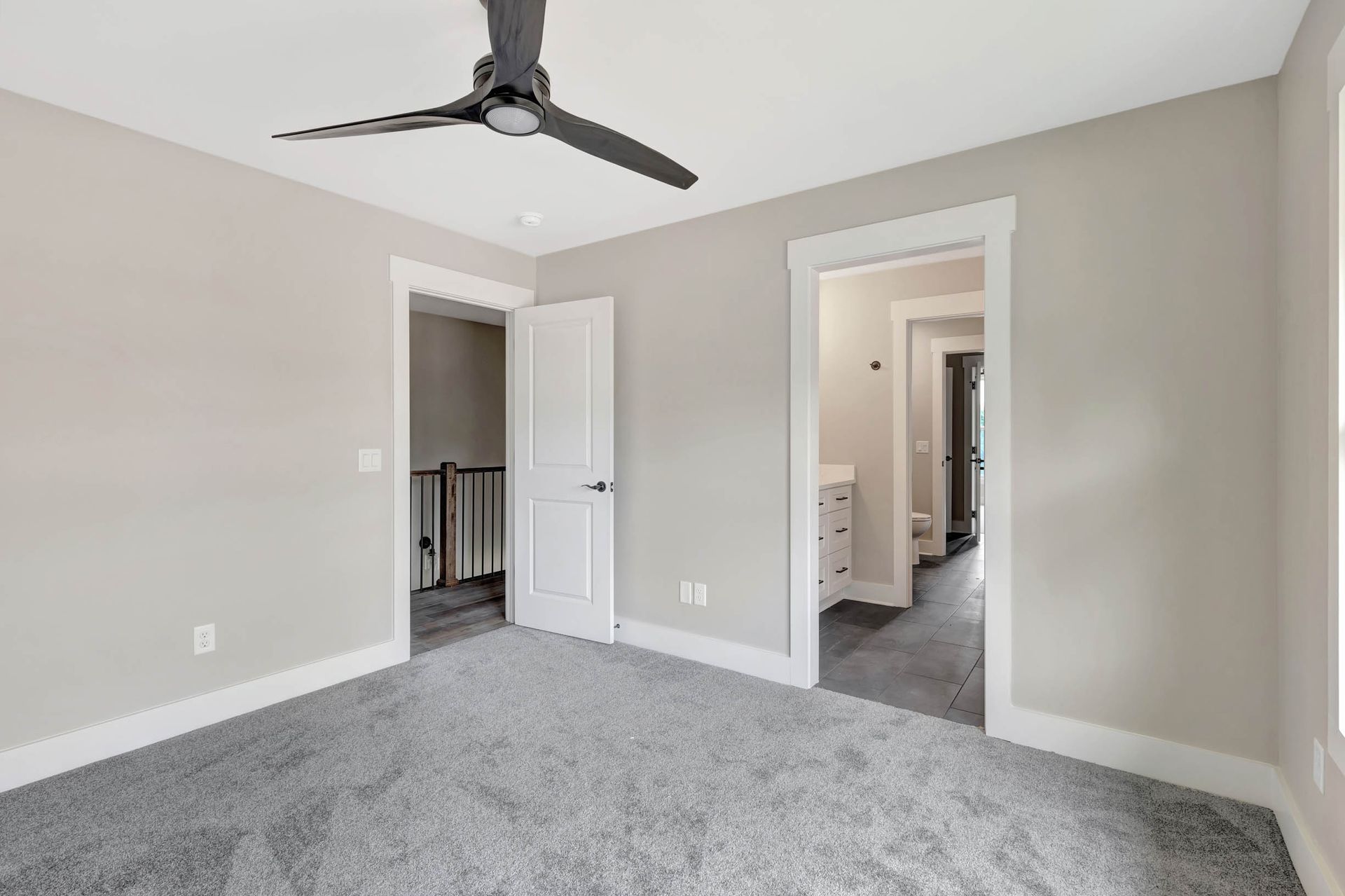 An empty bedroom with a ceiling fan and a gray carpet.