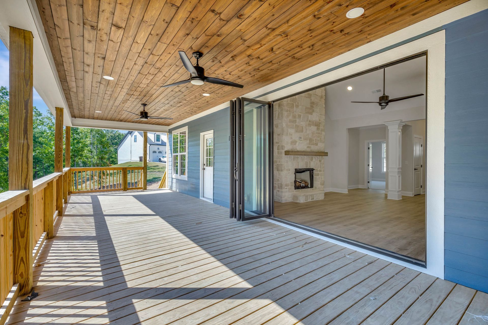 A large porch with a wooden ceiling and sliding glass doors leading to a living room.