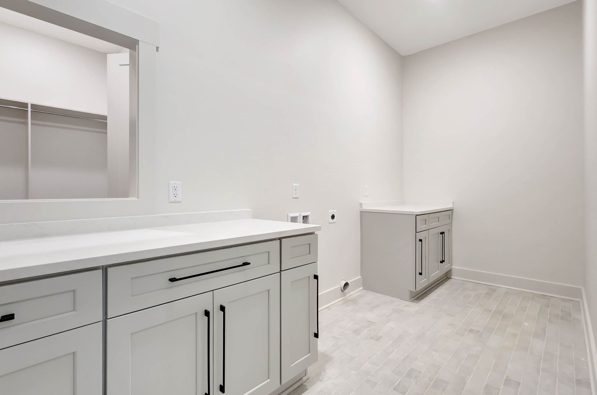 A laundry room with white cabinets and a window.