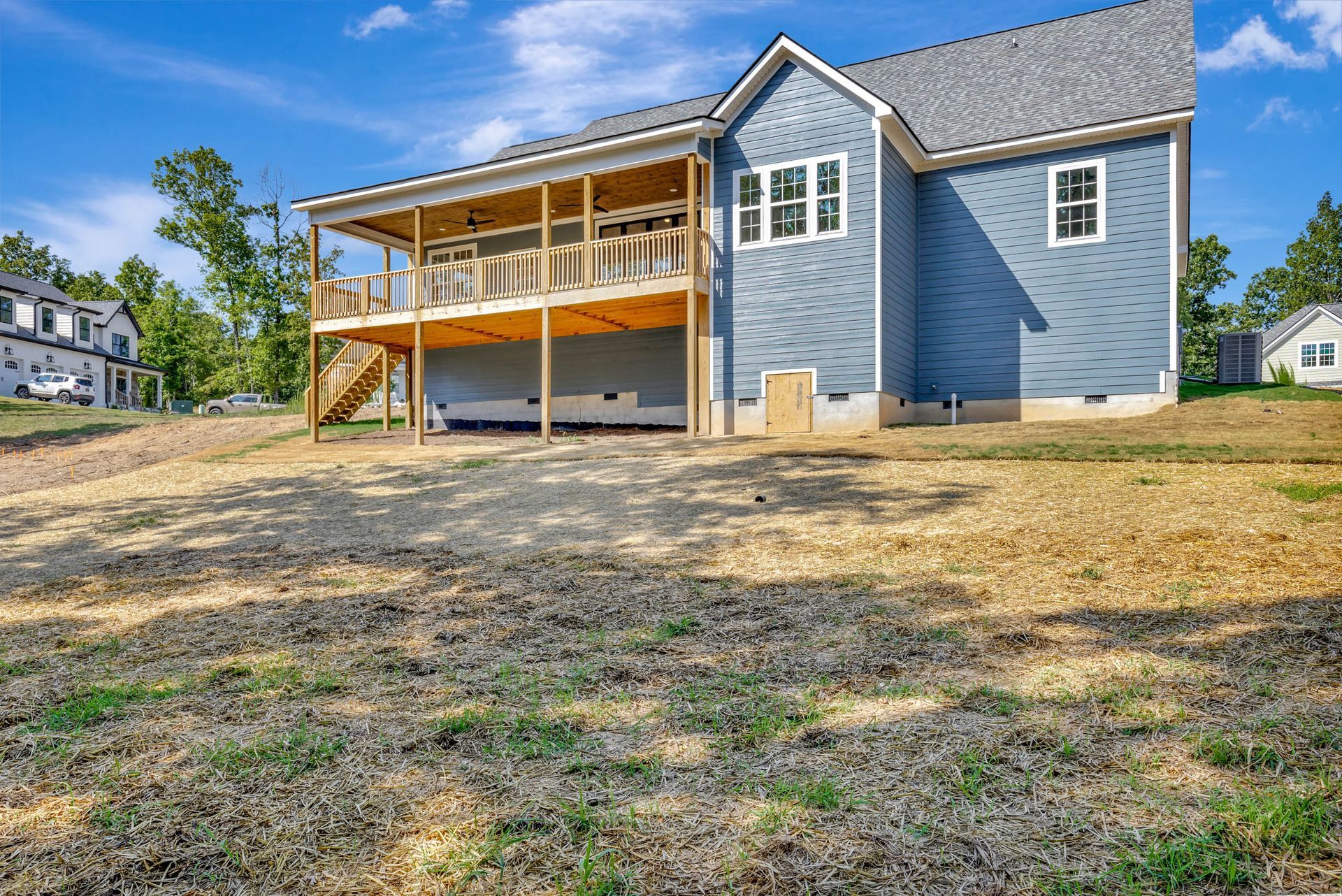 A blue house with a large deck is sitting on top of a dirt hill.
