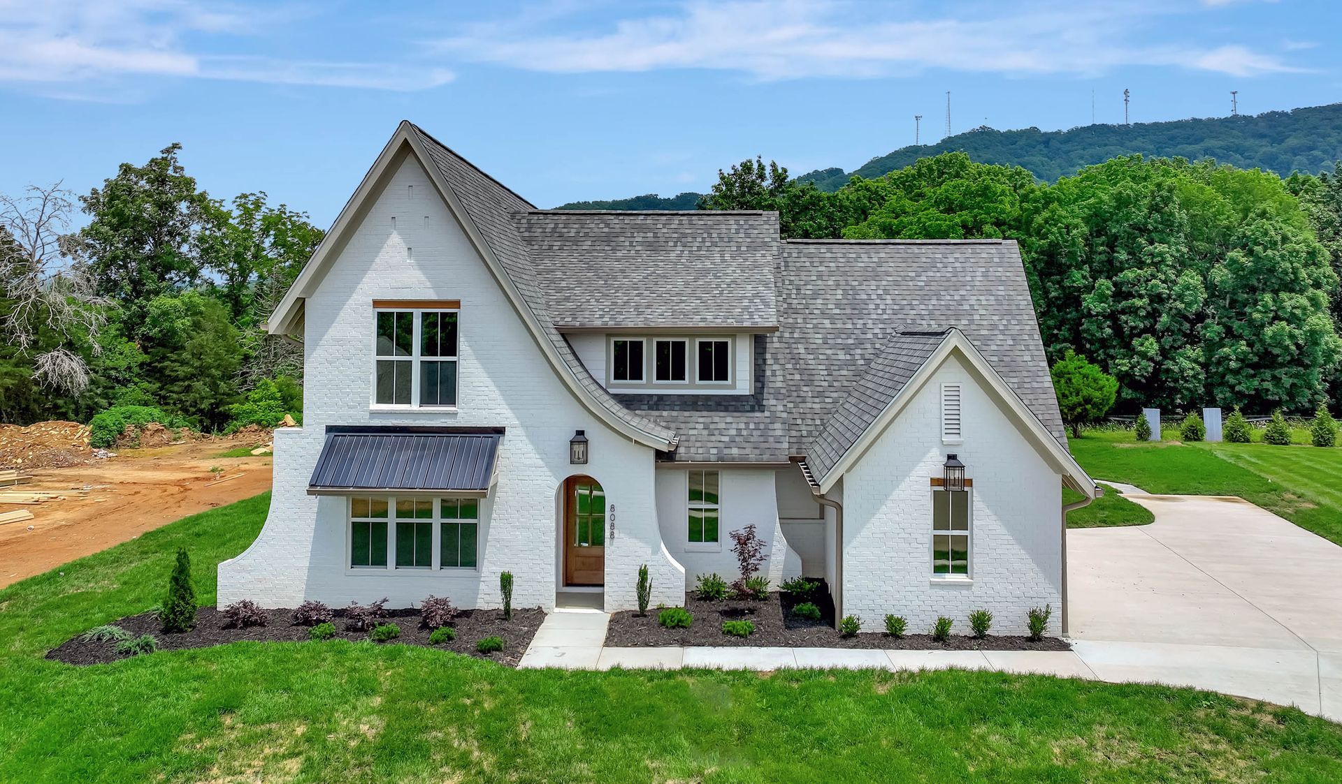 A white house with a gray roof is sitting on top of a lush green field.
