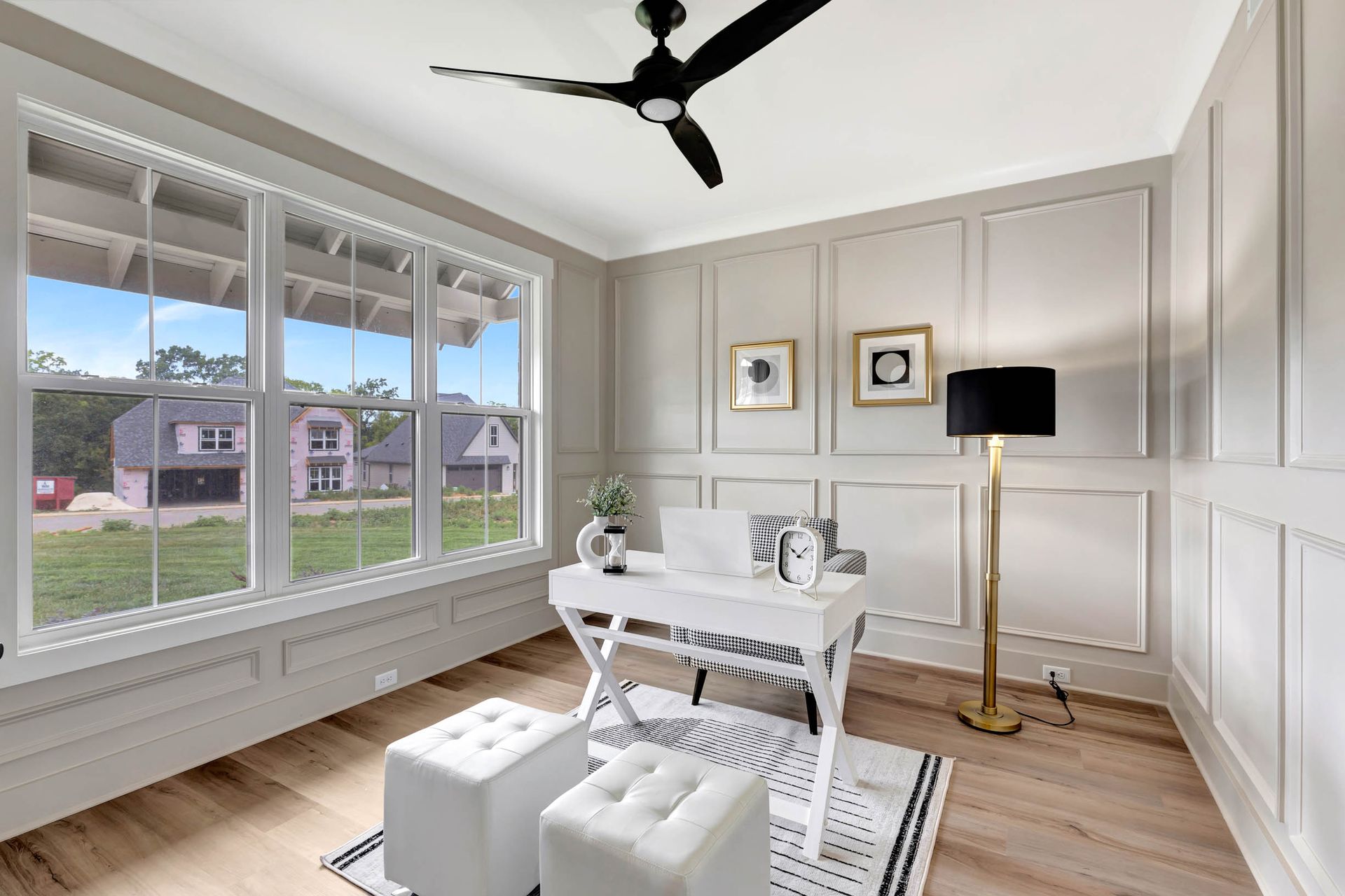 A home office with a desk , ottomans , and a ceiling fan.