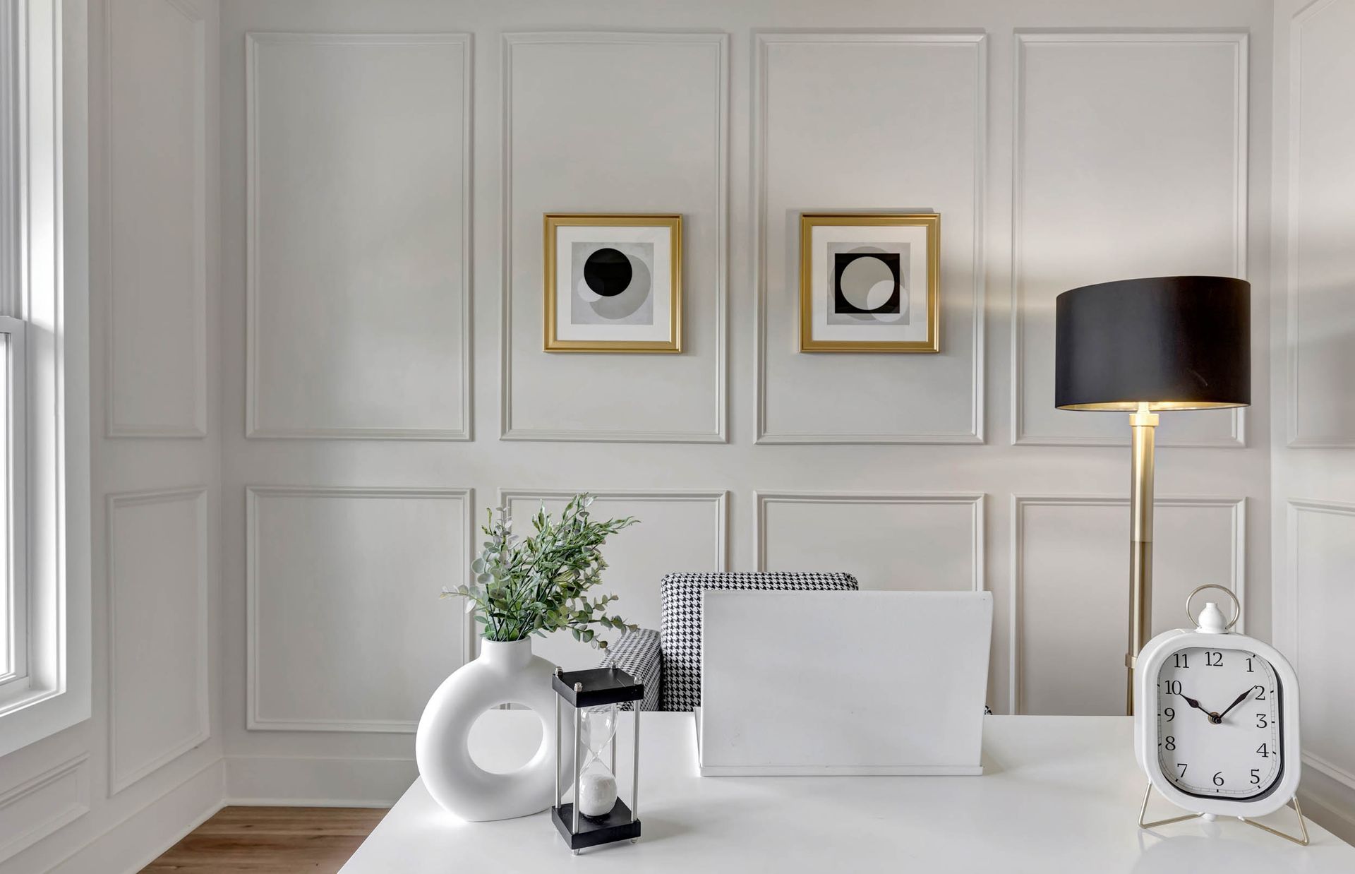 There is a desk with a laptop on it and a clock on it.