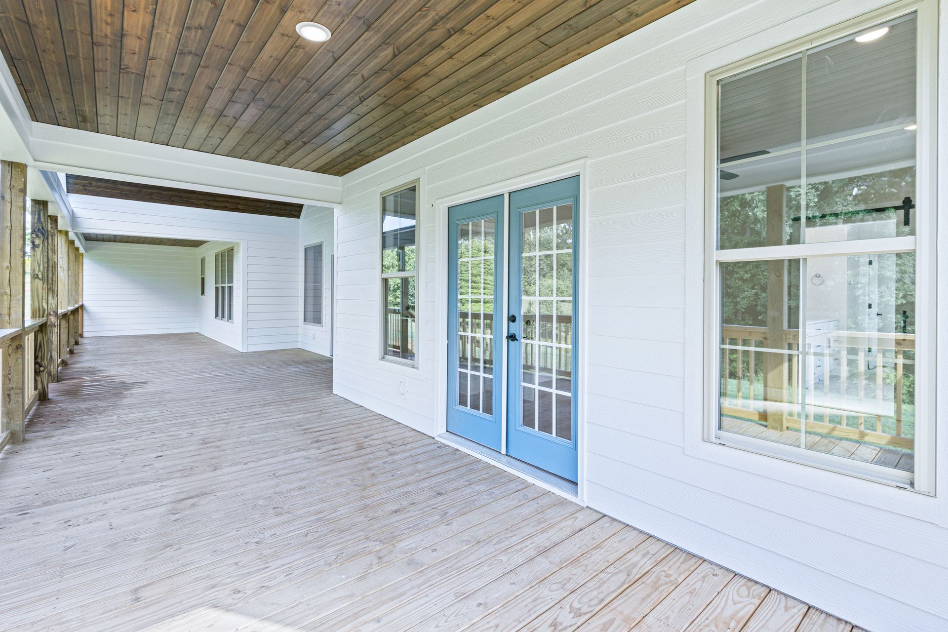 a large porch with blue french doors and a wooden ceiling .