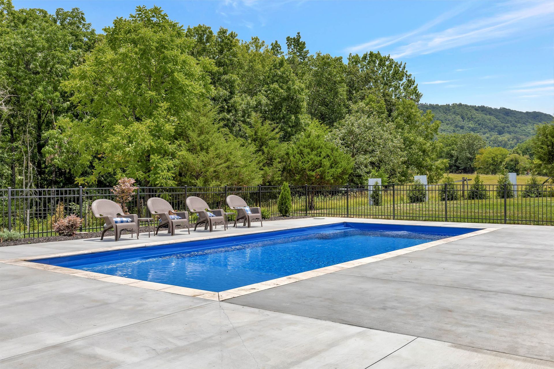 A large swimming pool surrounded by chairs and trees on a sunny day.