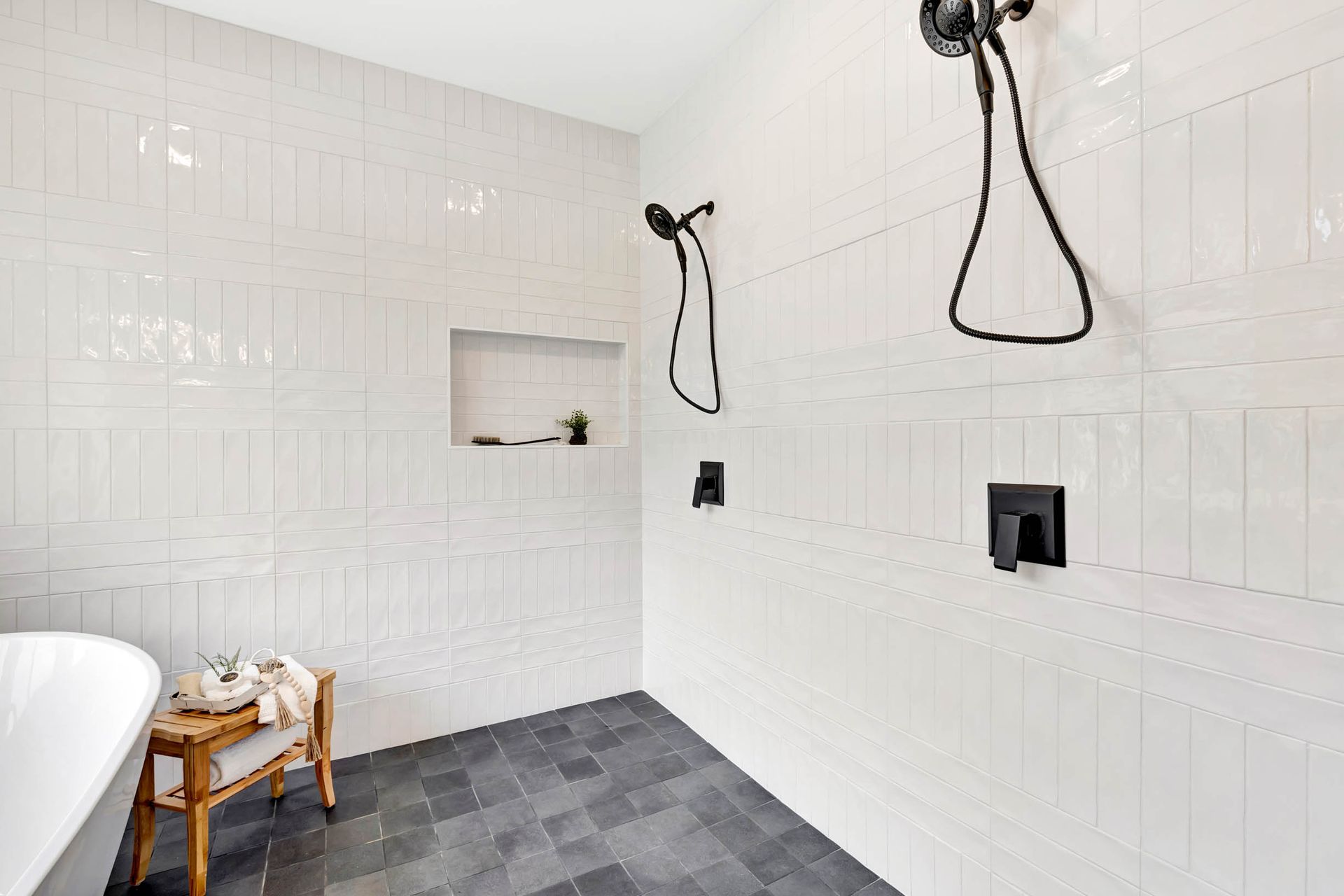 A bathroom with white tiles and black floors has a walk in shower and a bathtub.