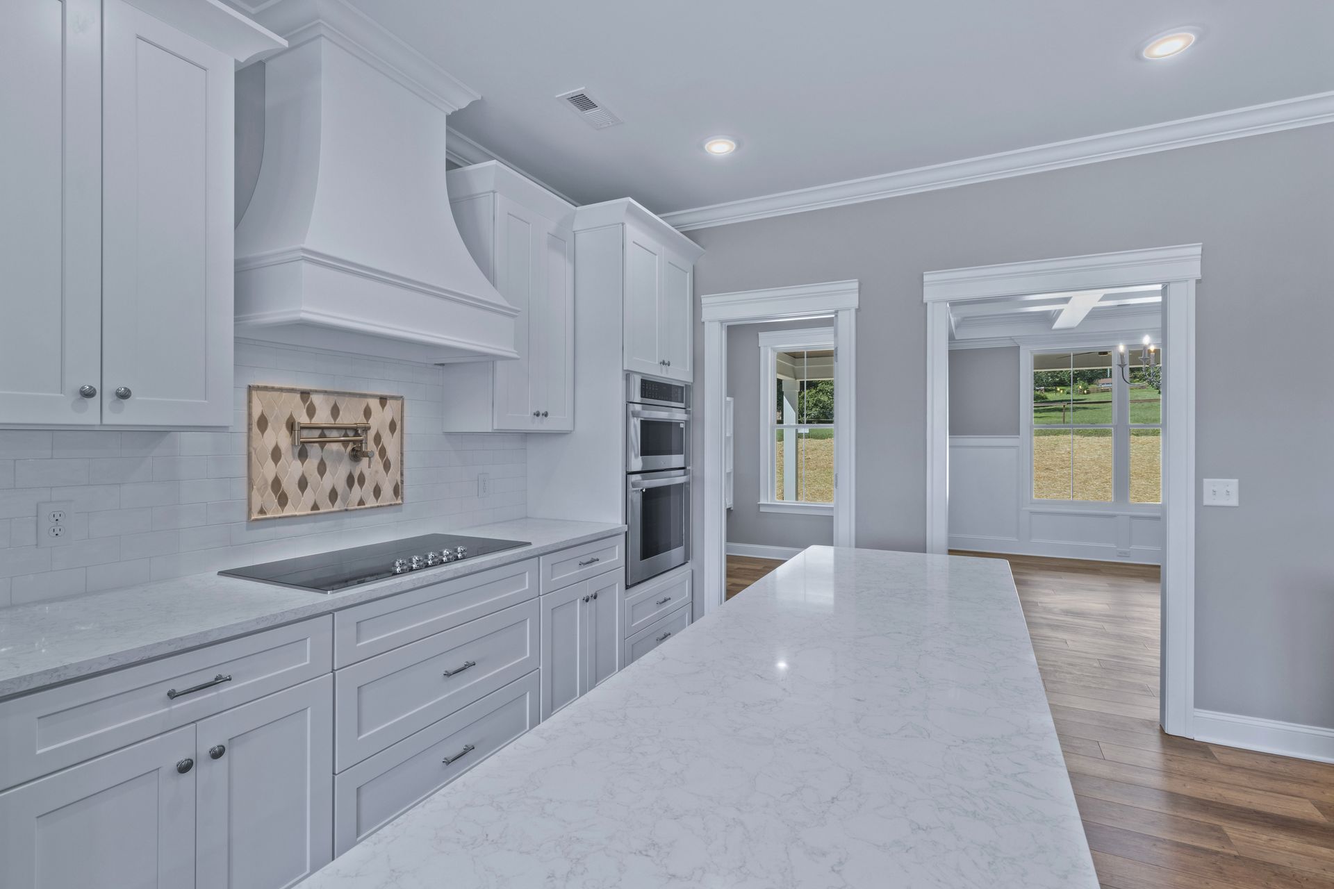 a kitchen with white cabinets , white counter tops , a stove , and a large island .