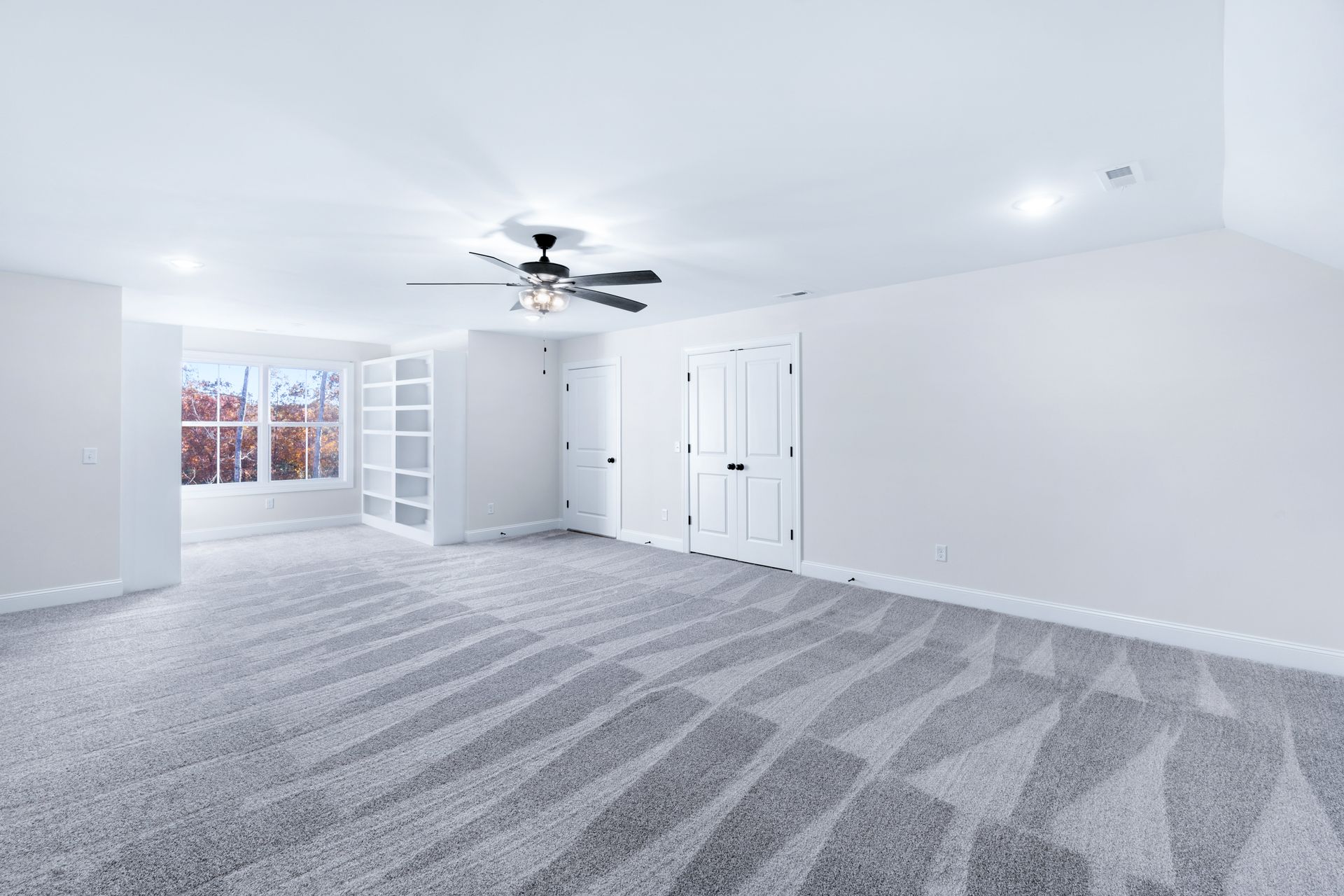 a large empty room with a ceiling fan and a gray carpet .
