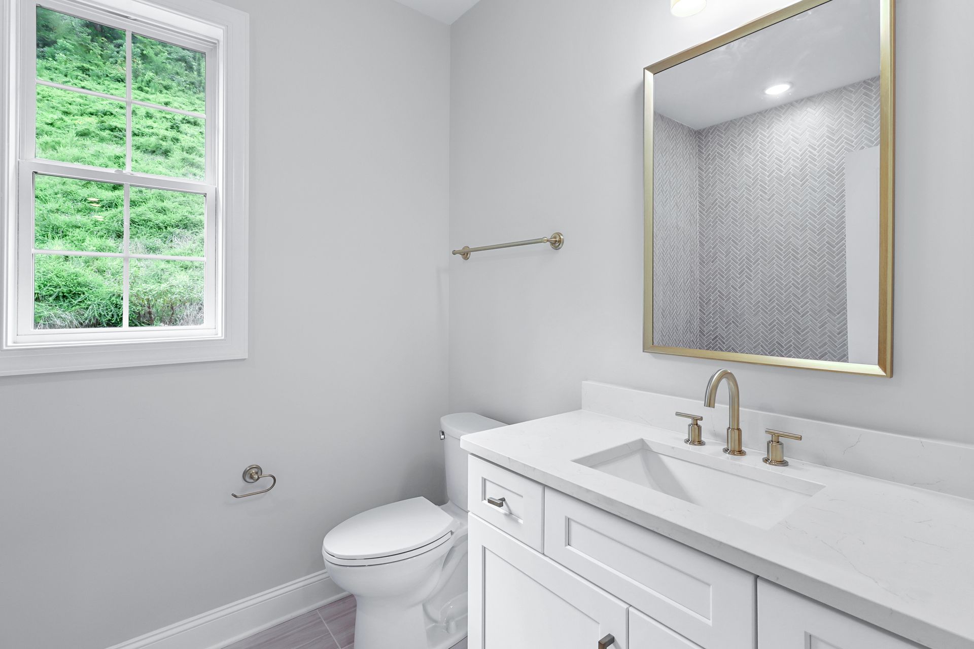 a bathroom with a toilet , sink , mirror and window .