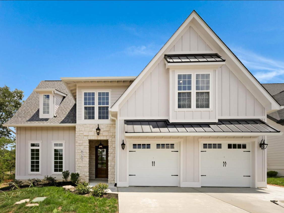 White farmhouse-style home with light stone accents, two-car garage, and blue sky.