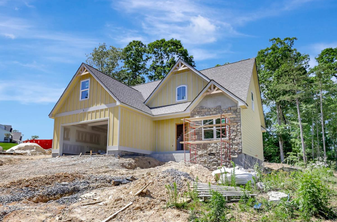 New house under construction with yellow siding, stone accents, and a garage.