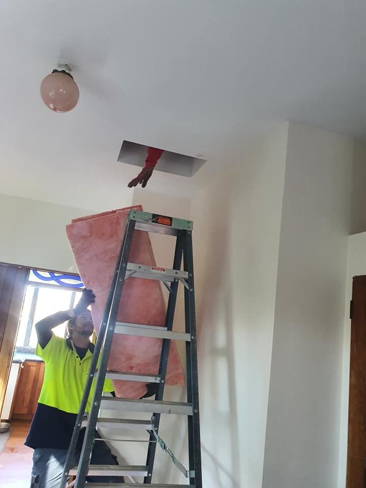 Worker on ladder fixing a ceiling opening, with a red panel and fluorescent lights indoors