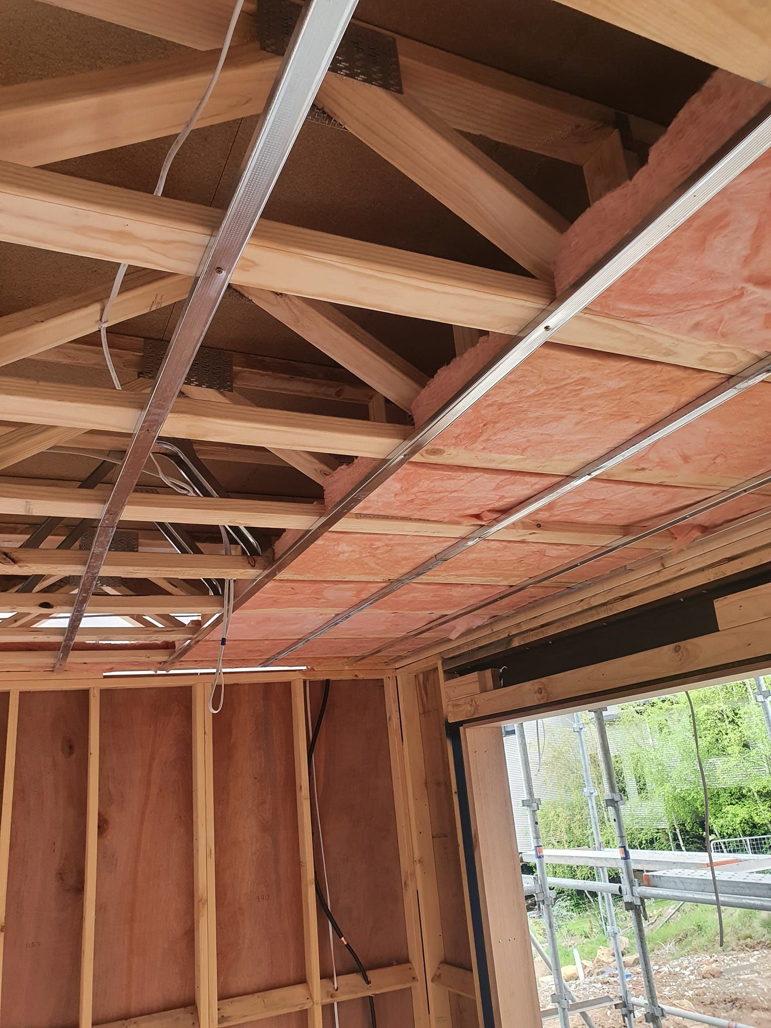 Interior of a wooden structure under construction, showing exposed roof trusses and insulation panels.
