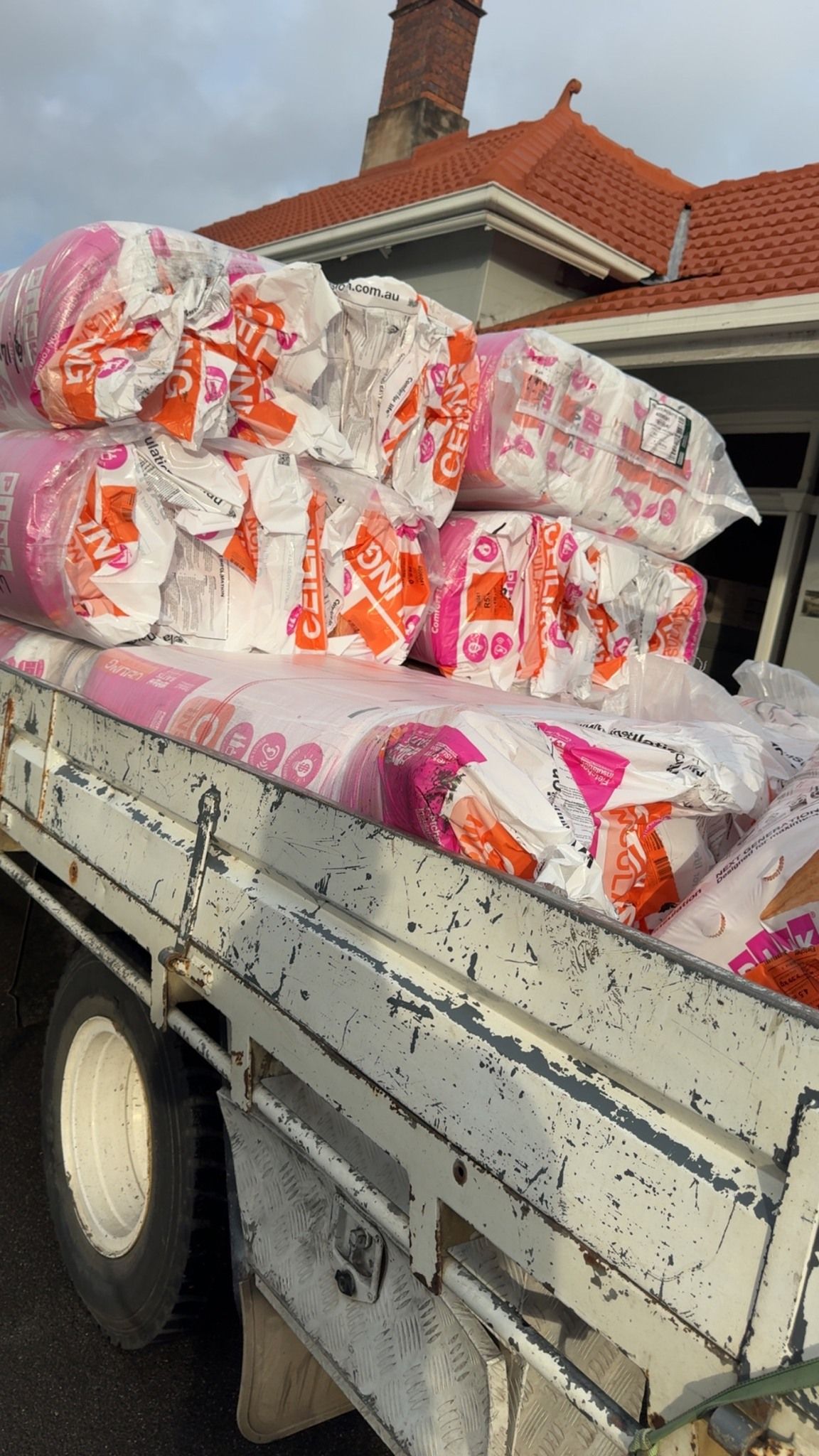 Truck bed loaded with stacked bags of supplies outside a house with a red-tile roof.