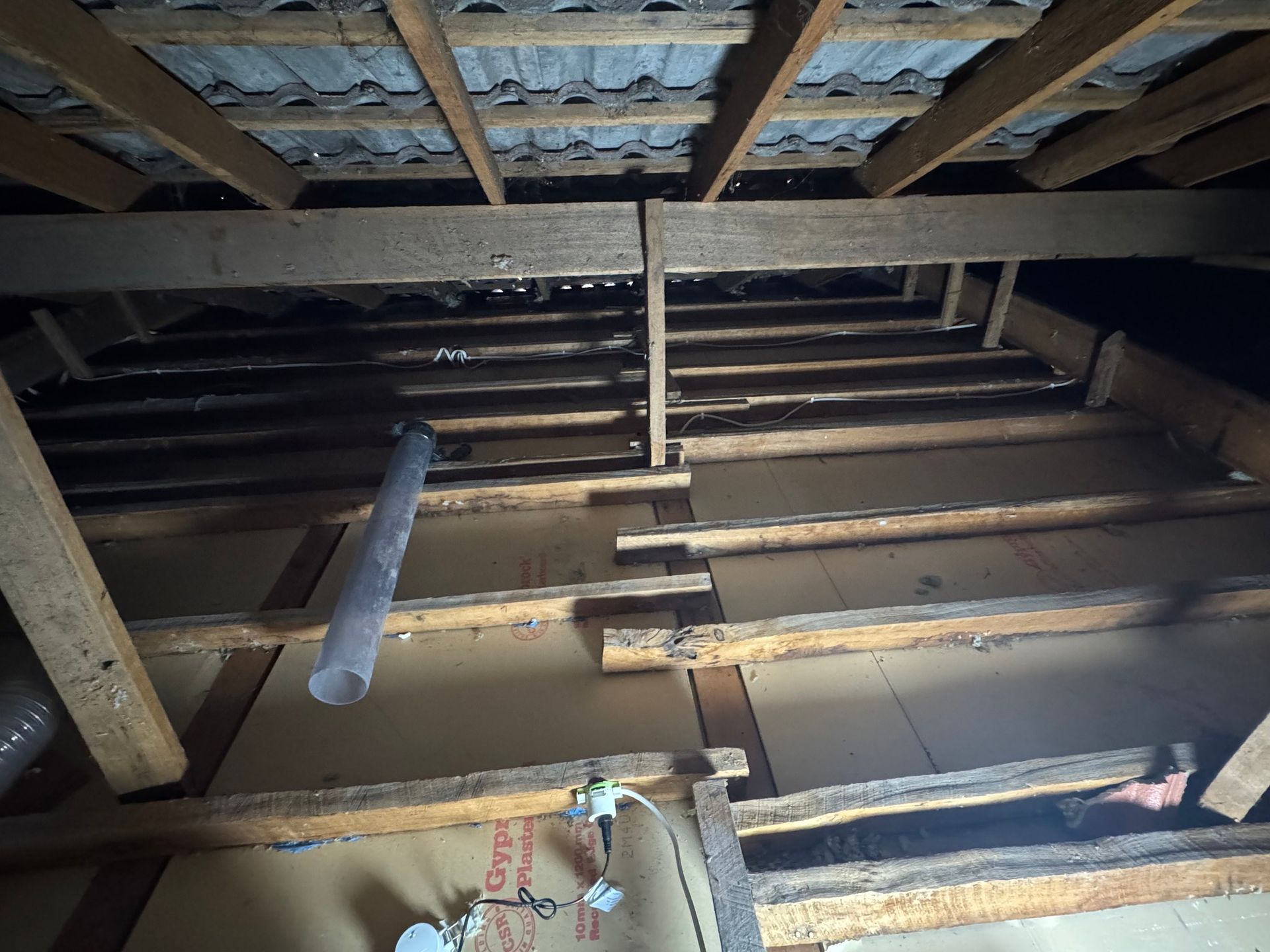 Inside an unfinished attic, exposed wooden beams and insulation are visible through a floor opening.