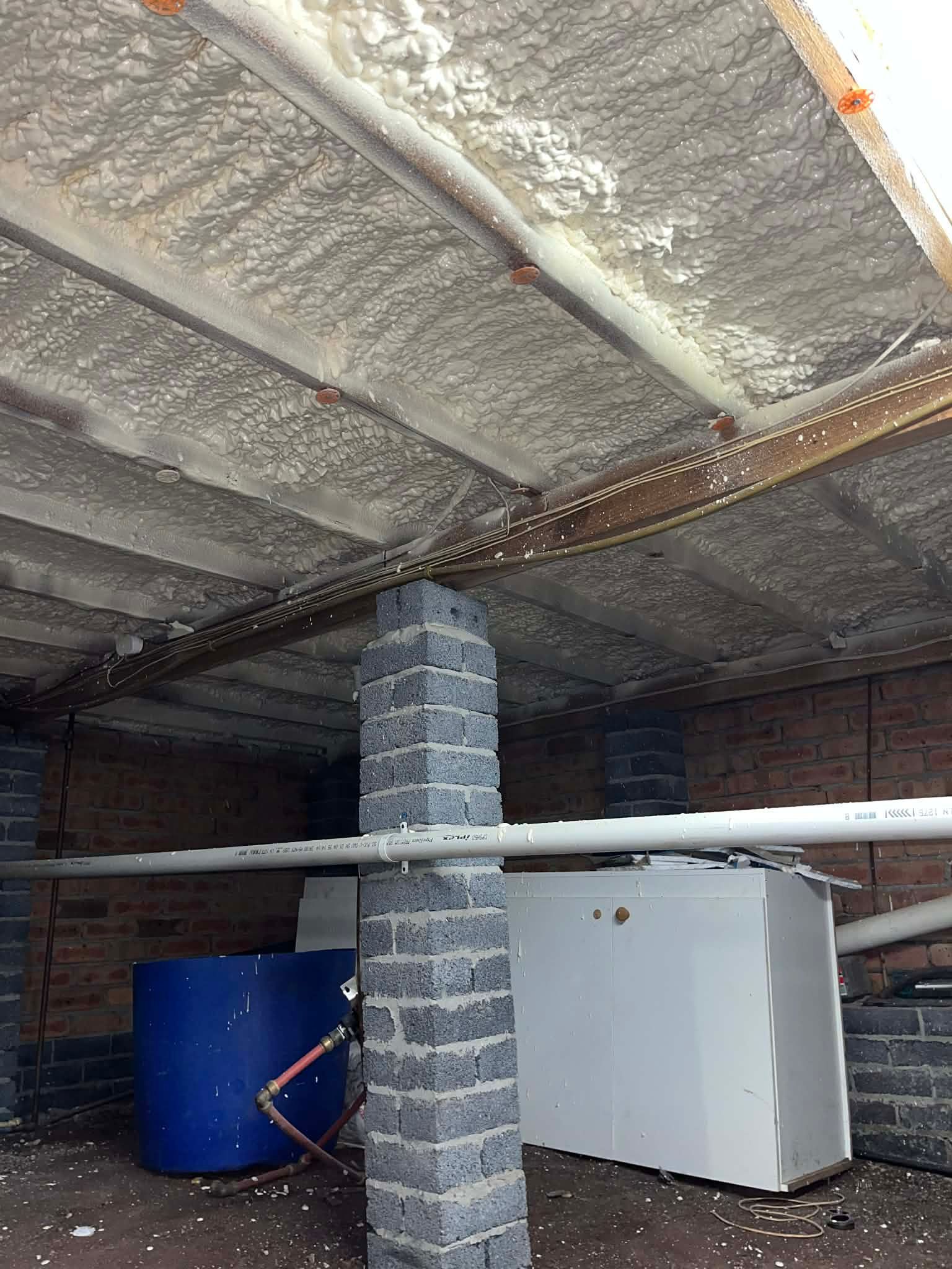 Basement with insulated ceiling, stone pillar, blue barrel, white cabinet, and wooden beams.