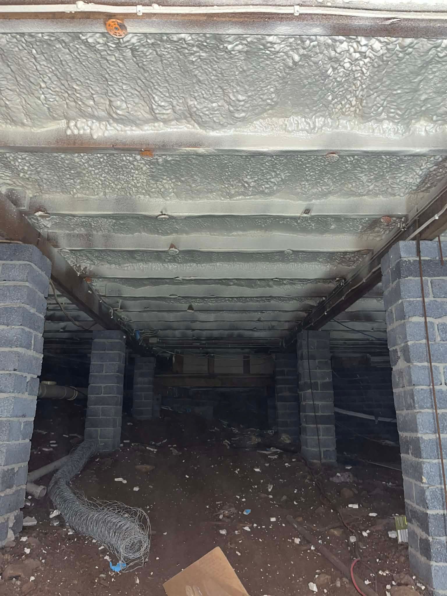 Abandoned concrete underpass with block pillars and debris-strewn dirt floor, seen from a dim entrance