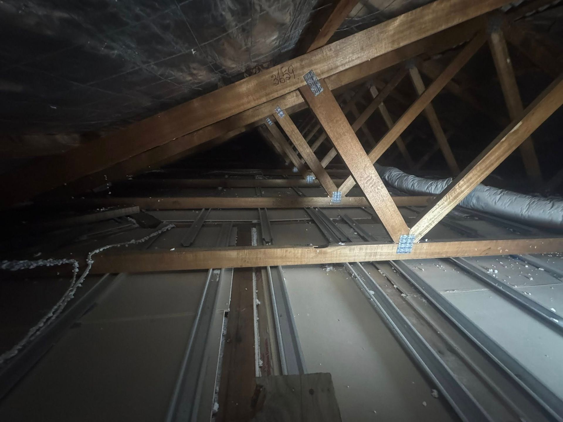 Wooden roof trusses in a dark attic with metal ductwork running below