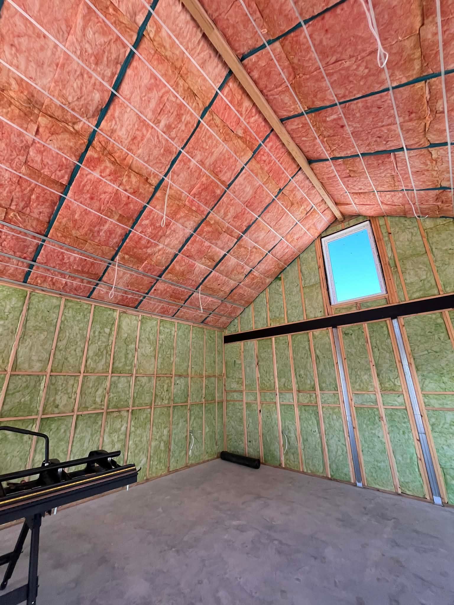 Unfinished attic room with insulated sloped walls, a small window, and concrete floor