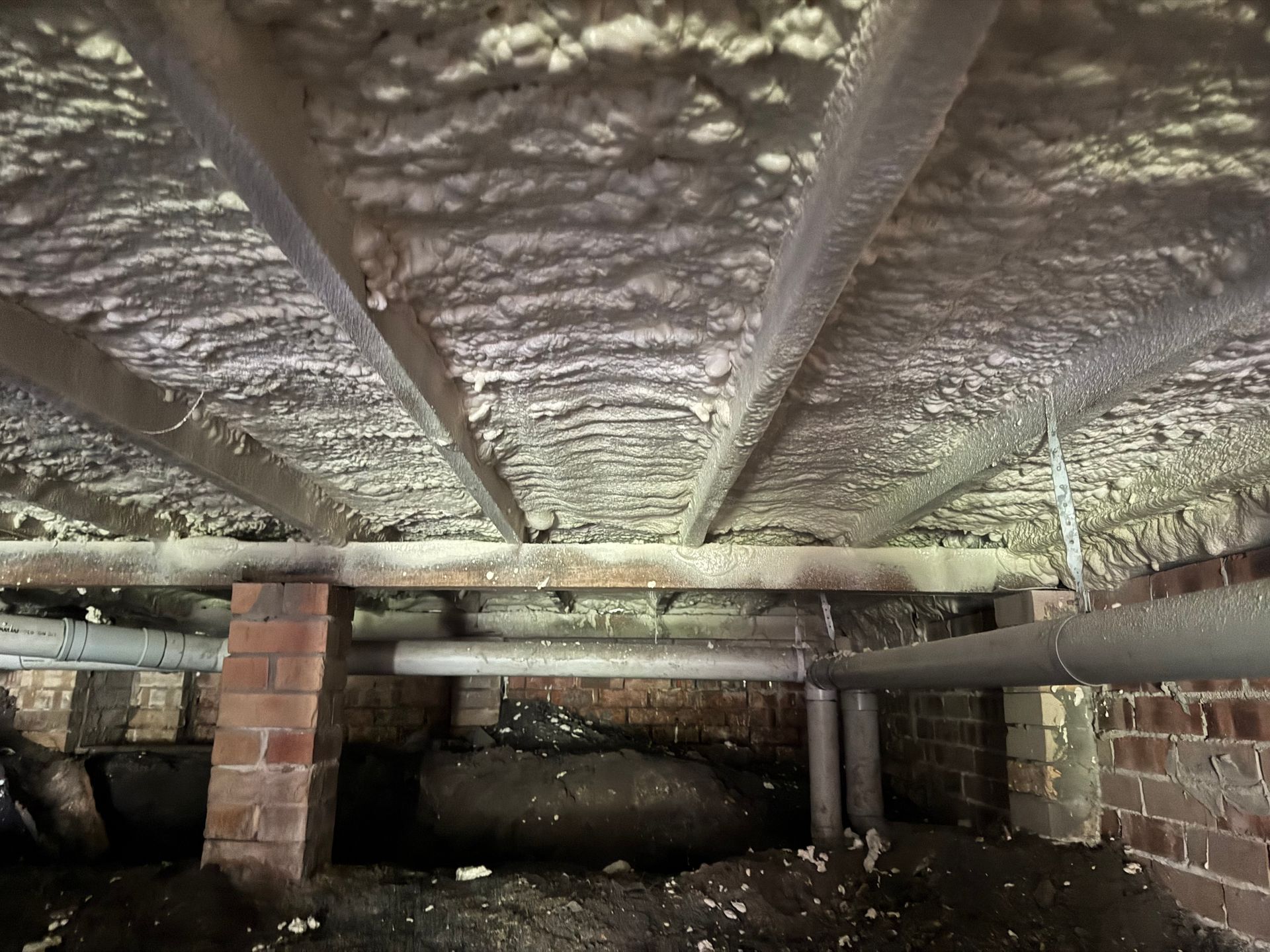 Under a raised wooden structure, showing insulation, support beams, and dirt ground below