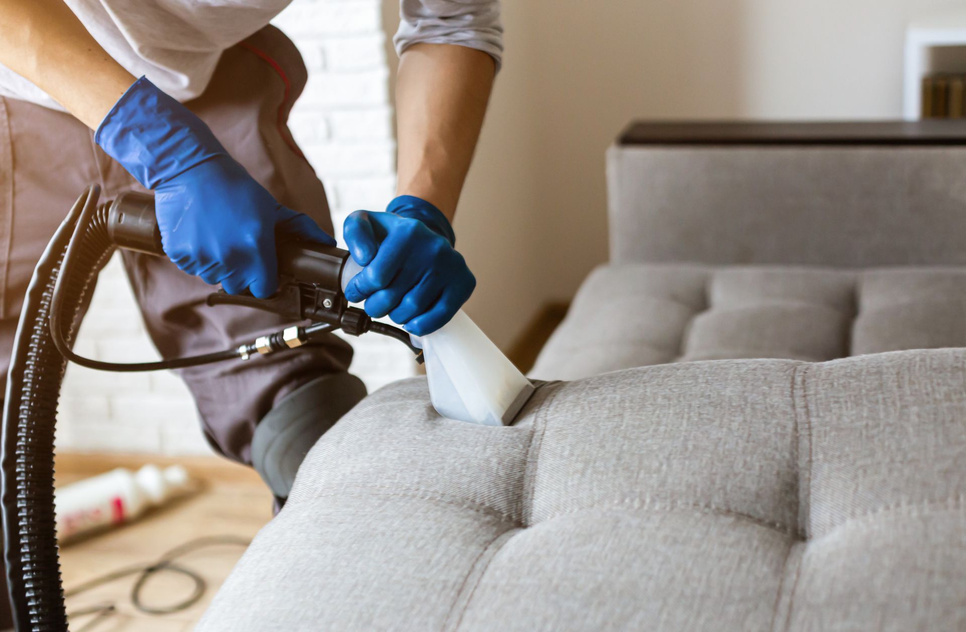 Close-up of an employee's hand in rubber gloves performing an upholstery cleaning service on a sofa.