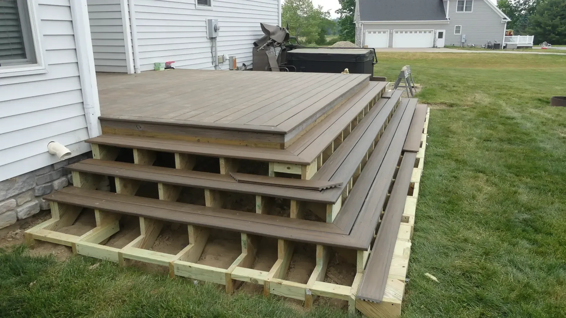 A partially finished wooden deck with three wide, open steps leading up to the main platform against a house exterior.