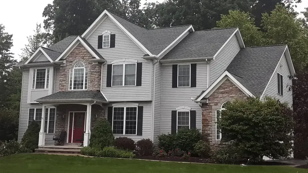 A two-story suburban house with light gray siding, a stone facade, a gabled roof, and a red front door.