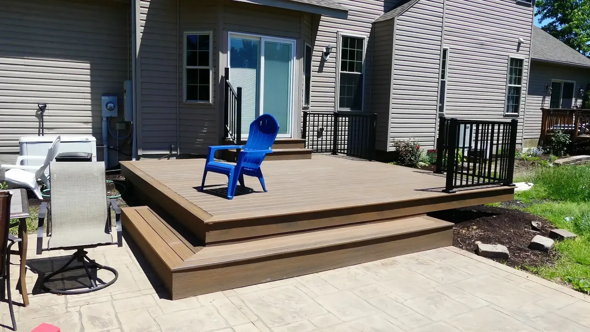 A brown wooden deck with steps leads to a sliding glass door, featuring a bright blue chair and a black metal railing.