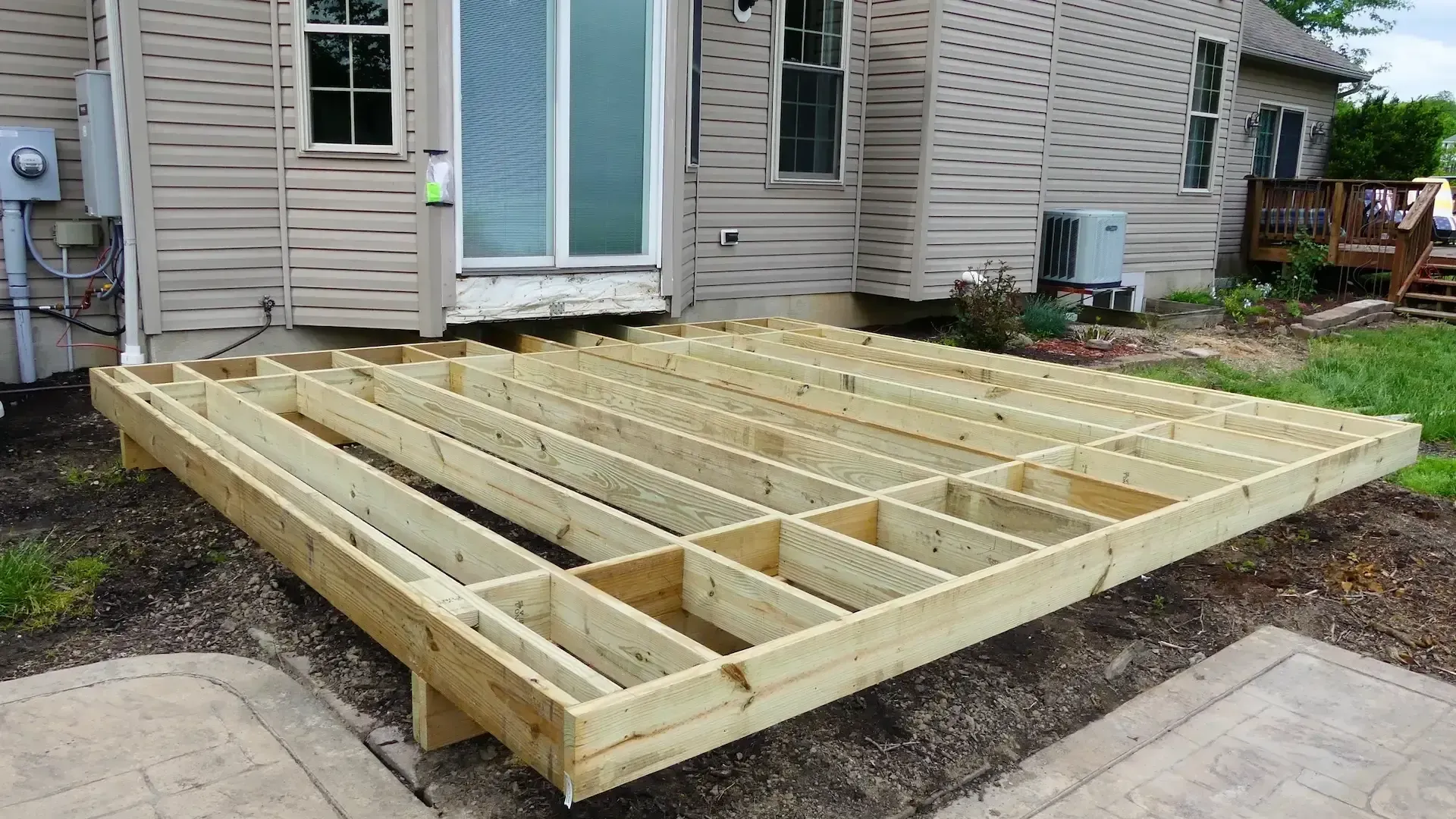 A wooden deck frame under construction attached to the back of a house.