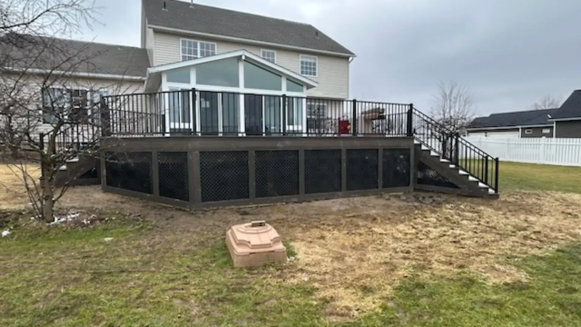 A two-story suburban house with a large composite deck featuring black railings and lattice skirting on a cloudy day.