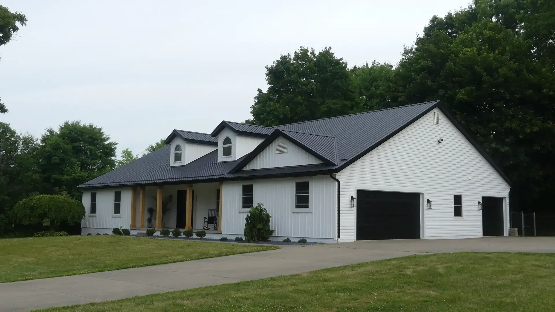 A single-story white house with a black roof, two dormers, a front porch, and an attached two-car garage on a lawn.