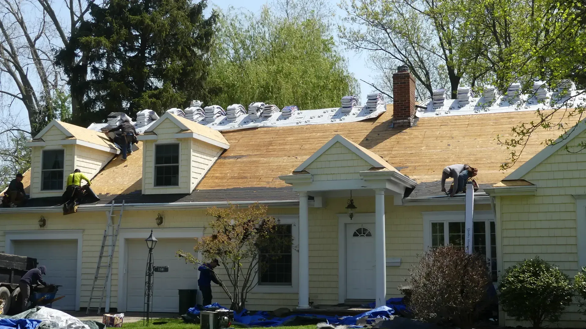Construction workers replacing the roof of a yellow house with a white garage and front porch.