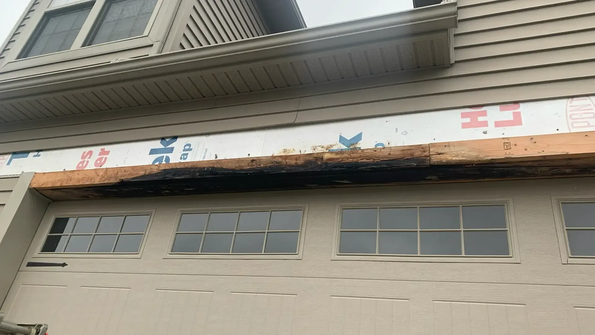 Exterior view of a residential garage door with a charred, damaged wooden header beam above the window panels.