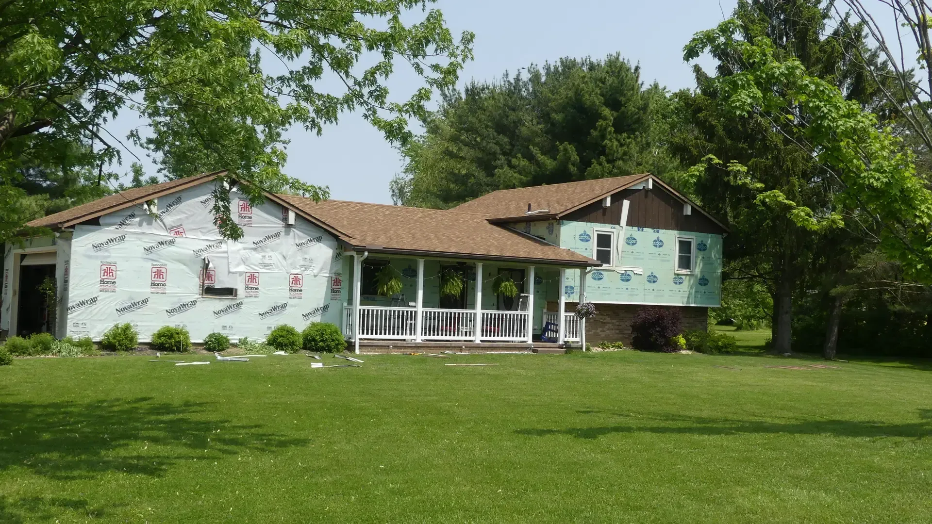 A ranch-style house with green underlayment, a brown roof, and a covered front porch, situated on a grassy lawn.