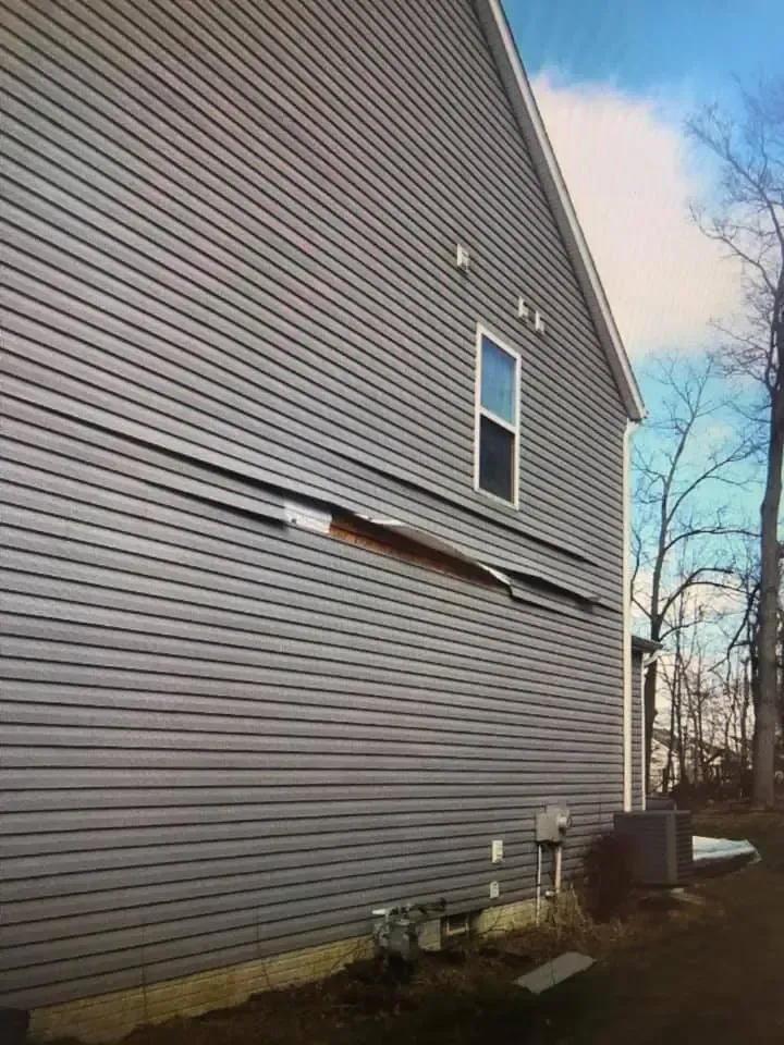 A side view of a gray-sided house with a horizontal section of siding detached and hanging from the wall.