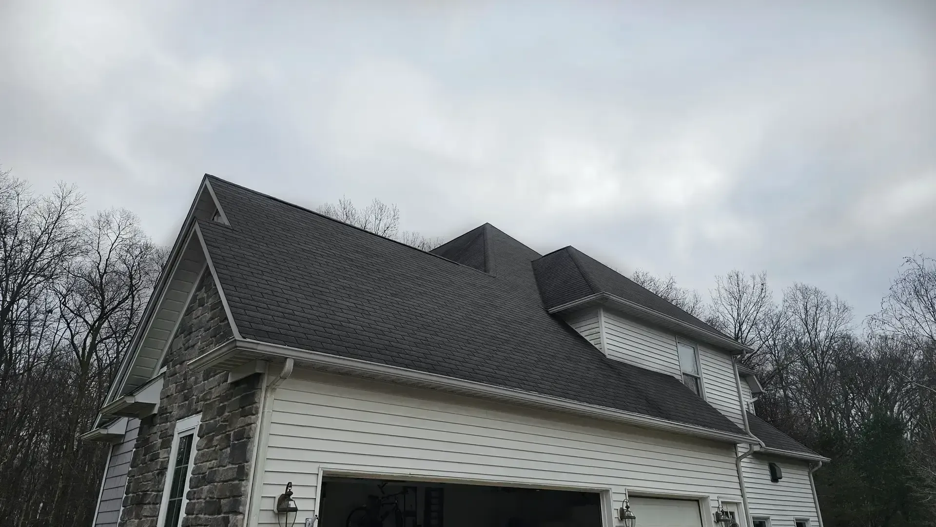 A two-story house with white siding and a stone exterior under a dark grey roof against a cloudy sky.