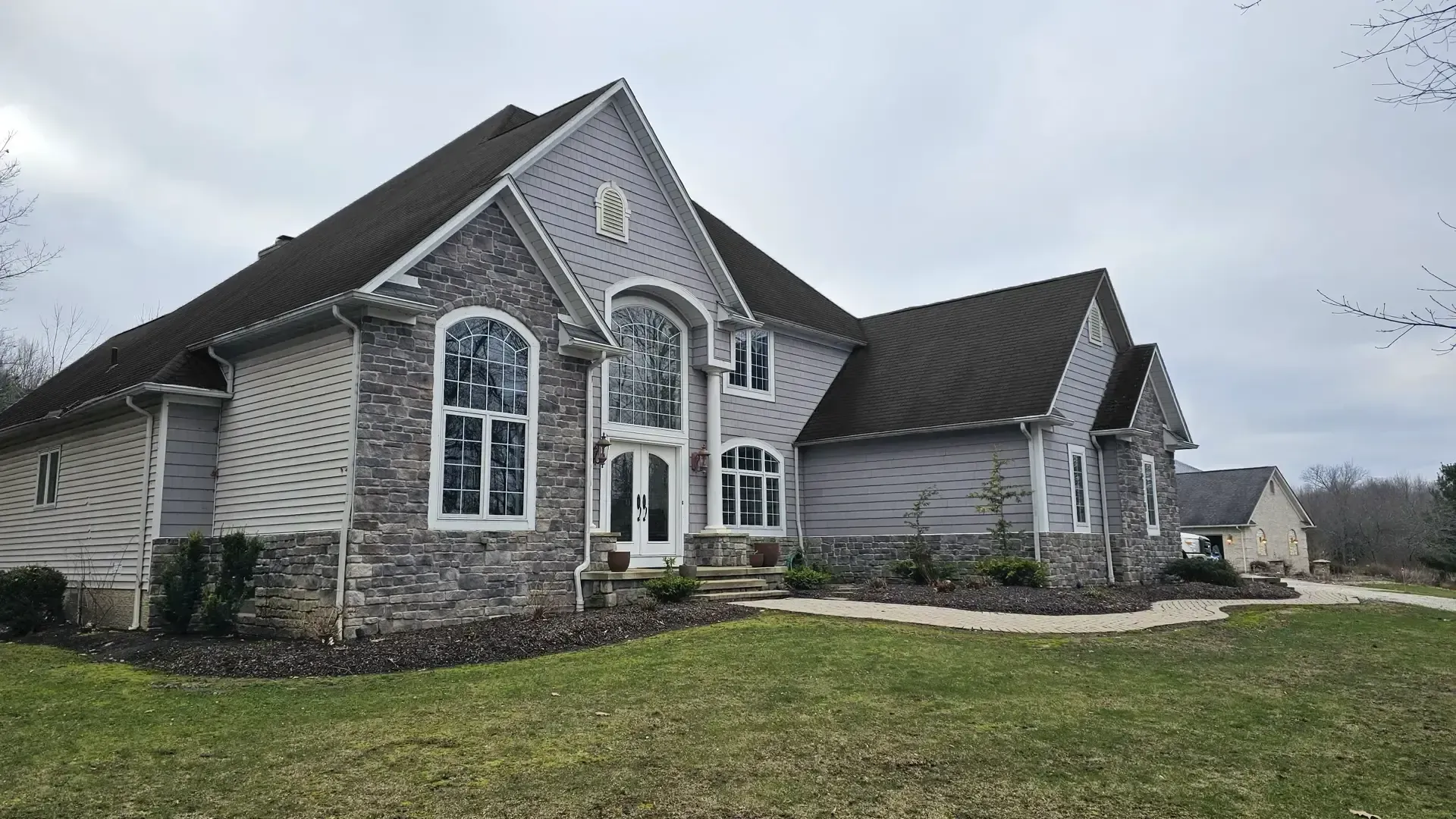 A two-story suburban house with stone and light-colored siding, a dark shingled roof, and a prominent front entrance.
