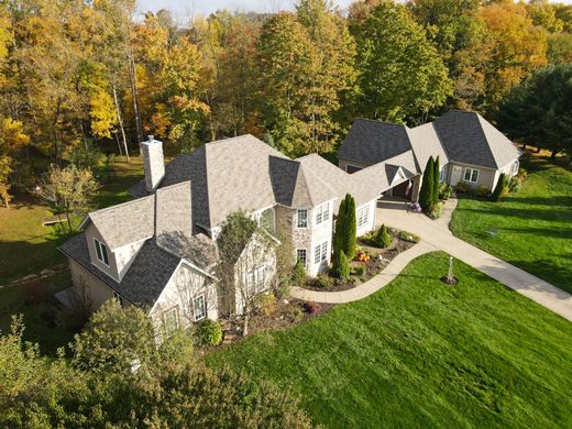 A single-story ranch house with a gray brick exterior, dark shingled roof, stone accents, and a lush front garden.